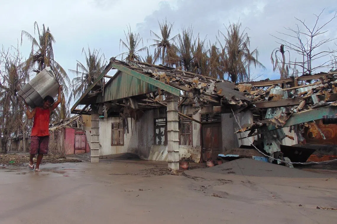A person carries his belongings as he walks past a damaged house affected by the eruption of Mount Ruang volcano in Laingpatehi village, Sitaro Islands Regency, North Sulawesi province, Indonesia, May 3, 2024. REUTERS/Chermanto Tjaombah