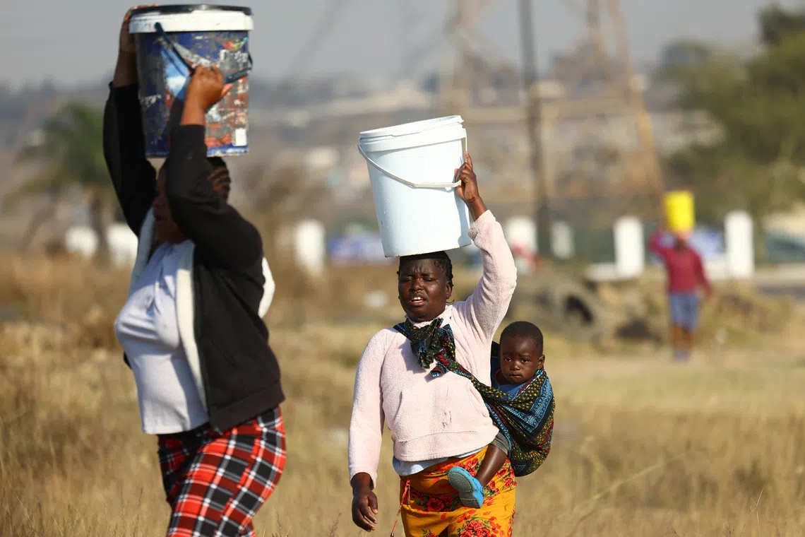 Residents carrying buckets filled with water collected from a nearby filling station in Olievenhoutbosch, north of Johannesburg, on Aug 7.