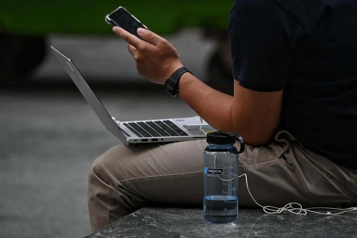 Um homem com seu laptop e telefone celular no Raffles Place MRT em 9 de fevereiro de 2022.