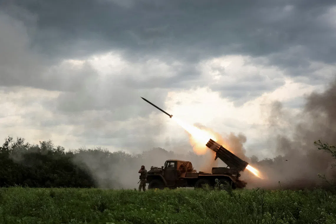 A military vehicle firing a rocket launcher in a field under a cloudy sky.