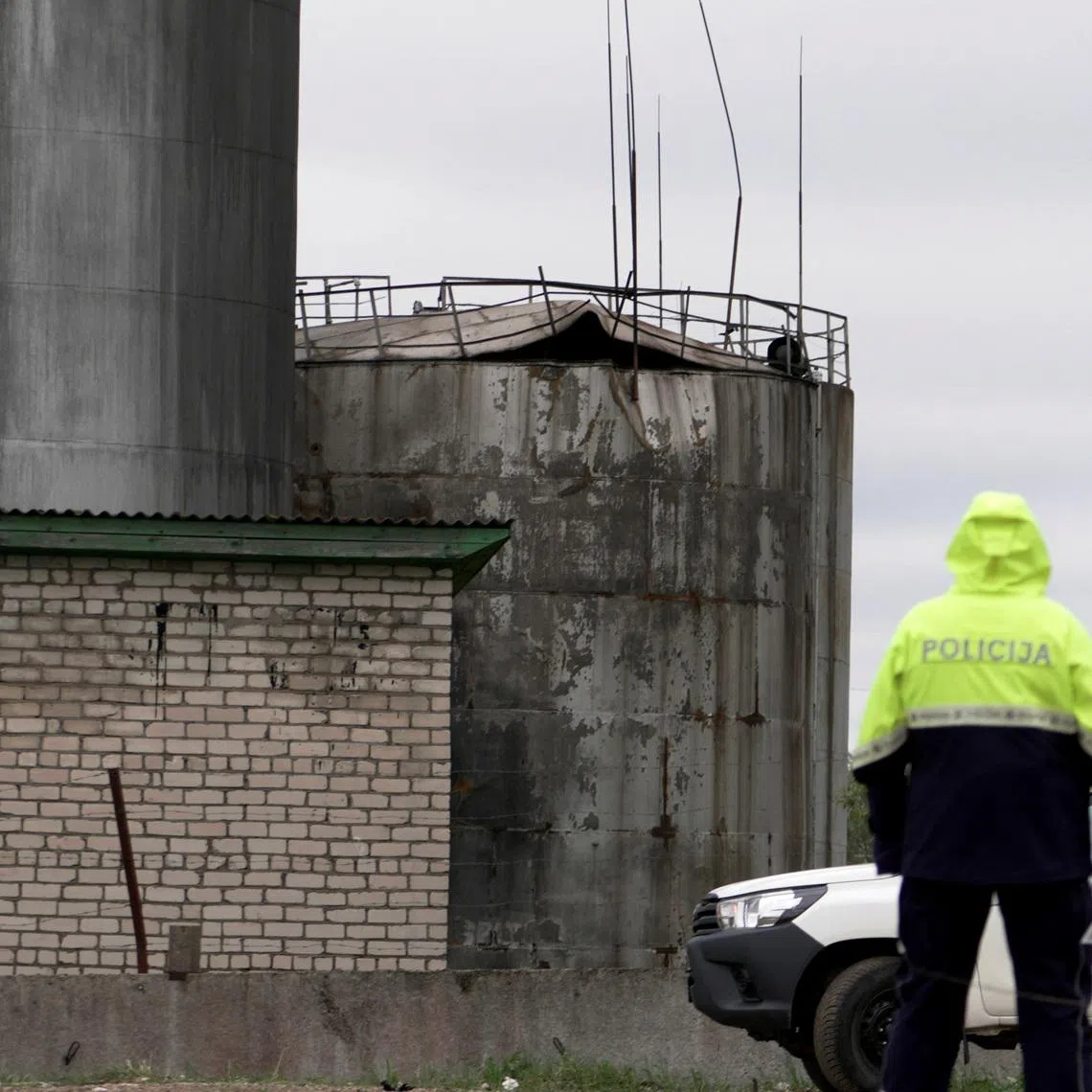 Police officer looks towards damage to an oil tank after drones crashed at a storage facility in Rezekne, Latvia, May 7, 2026. REUTERS/Janis Laizans