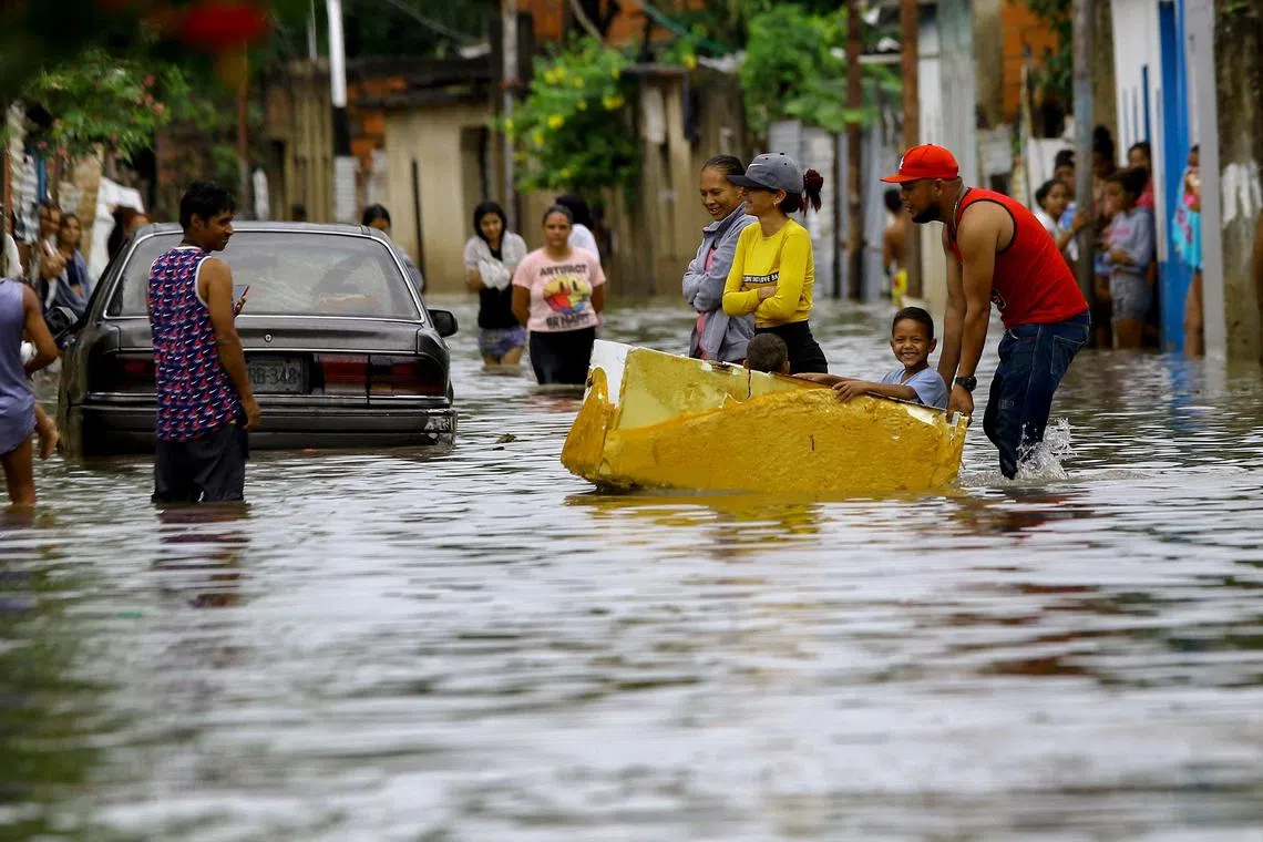 A man pushes an old refrigerator carrying two children in a flooded street after heavy rains caused by tropical waves affected several communities in the city of Valencia, Carabobo State, Venezuela, on May 30, 2023.