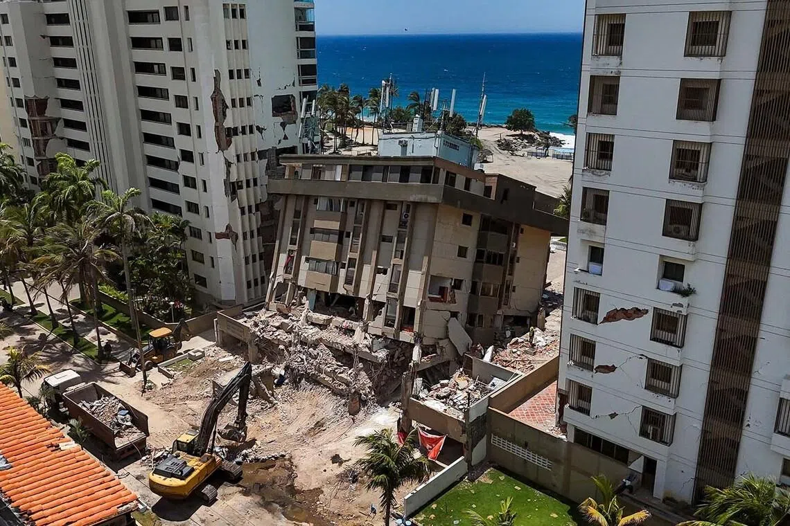 TOPSHOT - This aerial picture shows heavy machinery working on a residential building partially sunk into the ground near Playa Escondida in Tanaguarena, La Guaira state, Venezuela, on July 8, 2026. Venezuela's government called on July 8, 2026 for the release of frozen assets to help raise funds for the country's recovery from last month's twin earthquakes that killed at least 3,600 people. (Photo by Miguel MEDINA / AFP)