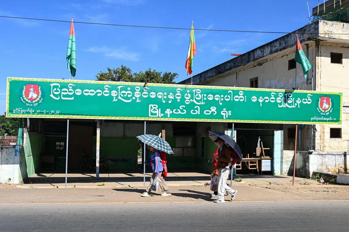People walk past an election campaign billboard ahead of Myanmar's general election in Nawnghkio in Myanmar’s northern Shan State, on Dec 9, 2025.