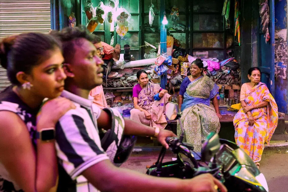 Women sitting outside a footwear stall as traffic passes along a street in Kolkata, India, on Sept 29, 2025. 