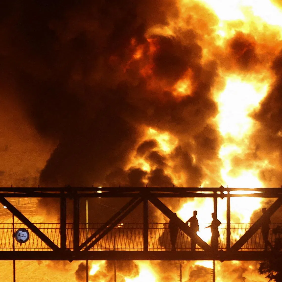 People watch from a bridge as flames from an Israeli attack rise from Sharan Oil depot, following Israeli strikes on Iran, in Tehran, Iran, June 15, 2025. Majid Asgaripour/WANA (West Asia News Agency) via REUTERS