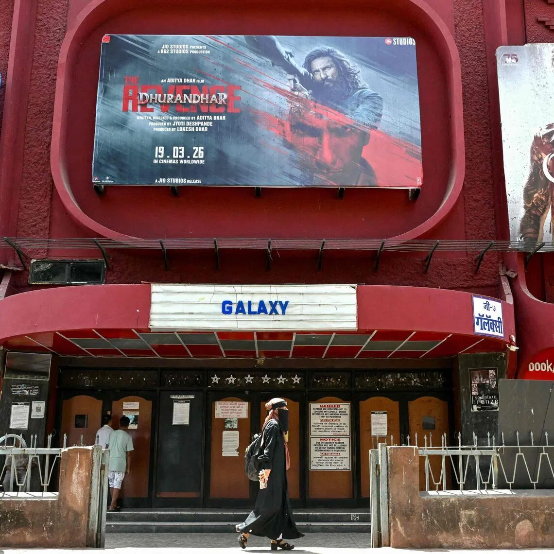 A woman walks past a poster of Indian Hindi-language spy action thriller film Dhurandhar: The Revenge (C), displayed outside a movie theatre in Mumbai on April 7, 2026. (Photo by Indranil MUKHERJEE / AFP)