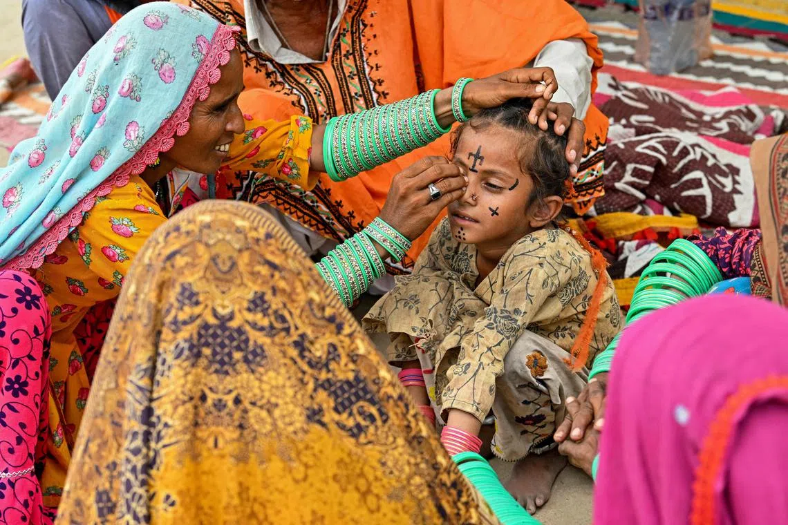 Artist Guddi Manthar (L), drawing an indigenous tattoo on seven-year-old Champa's face at the Jogi Colony in Umerkot.