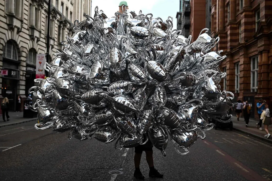 A ballon seller carrying inflatable trophies as he arrives on site of the Manchester City's victory parade for European Cup, the FA Cup and the Premier League, in the streets of Manchester, northern England on June 12, 2023. Manchester City tasted Champions League glory at last on Saturday as a second-half Rodri strike gave the favourites a 1-0 victory over Inter Milan in a tense final, allowing Pep Guardiola's side to complete a remarkable treble. Having already claimed a fifth Premier League title in six seasons, and added the FA Cup, City are the first English club to win such a treble since Manchester United in 1999. 