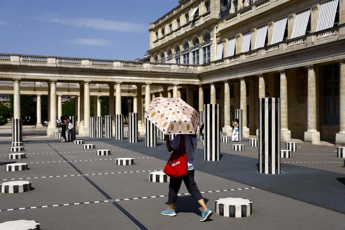 Paris 2024 Olympics - Paris, France - July 30, 2024 A person walks past the Buren columns at Paris Domaine National du Palais-Royal with an umbrella during hot weather in Paris REUTERS/Abdul Saboor