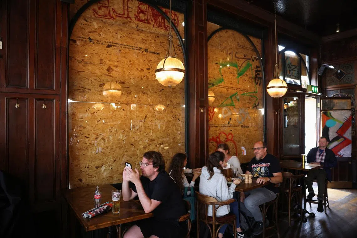 FILE PHOTO: People sit inside a boarded up pub in London, Britain, August 26, 2023. REUTERS/Hollie Adams/File Photo
