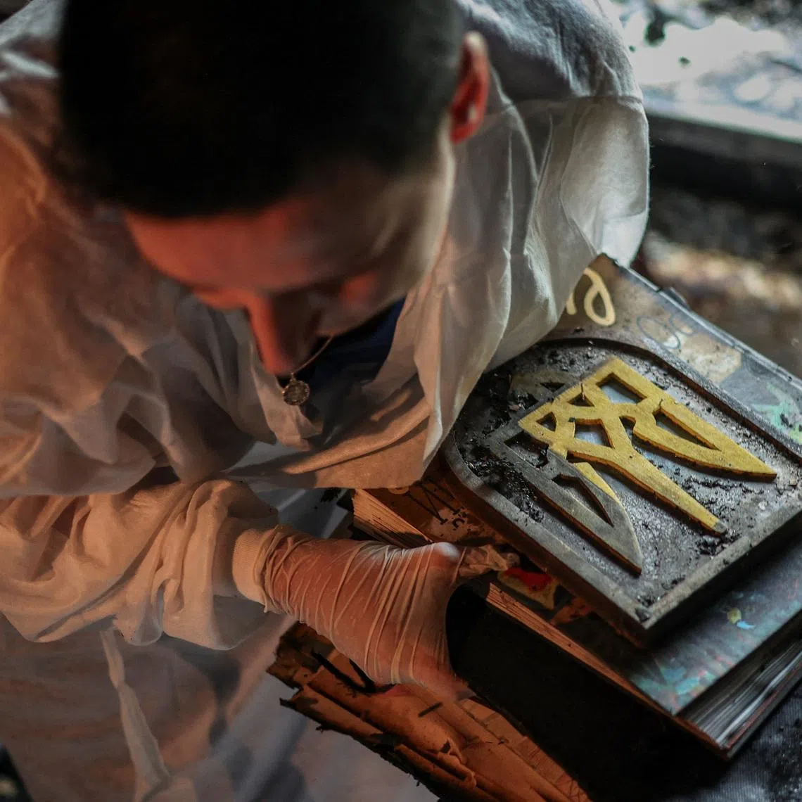 Iryna Plekhova, 42, resident who survived yesterday's Russian missile and drone attack, carries her remaining personal belongings and partially damaged Ukrainian coat of arms, the tryzub, carved out of wood by her father-in-law, in the burned down apartment, which was damaged during the strike, amid Russia's attack on Ukraine, in Kyiv, Ukraine July 3, 2026. REUTERS/Alina Smutko