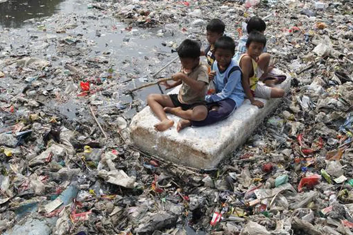 Children sitting on a makeshift raft play in a river full of rubbish in a slum area of Jakarta on Sept 19, 2012.