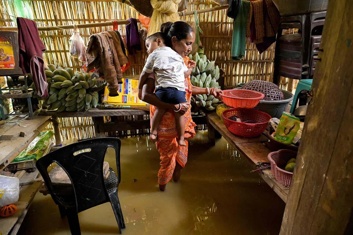 A woman holding a child as she collects her belongings from inside a flooded house, after heavy rains in Kampur, in India's northeastern state of Assam on June 2, 2025. Flash floods and landslides after torrential monsoon rain over the last two days killed at least 30 people in India's northeast, officials said on June 1.