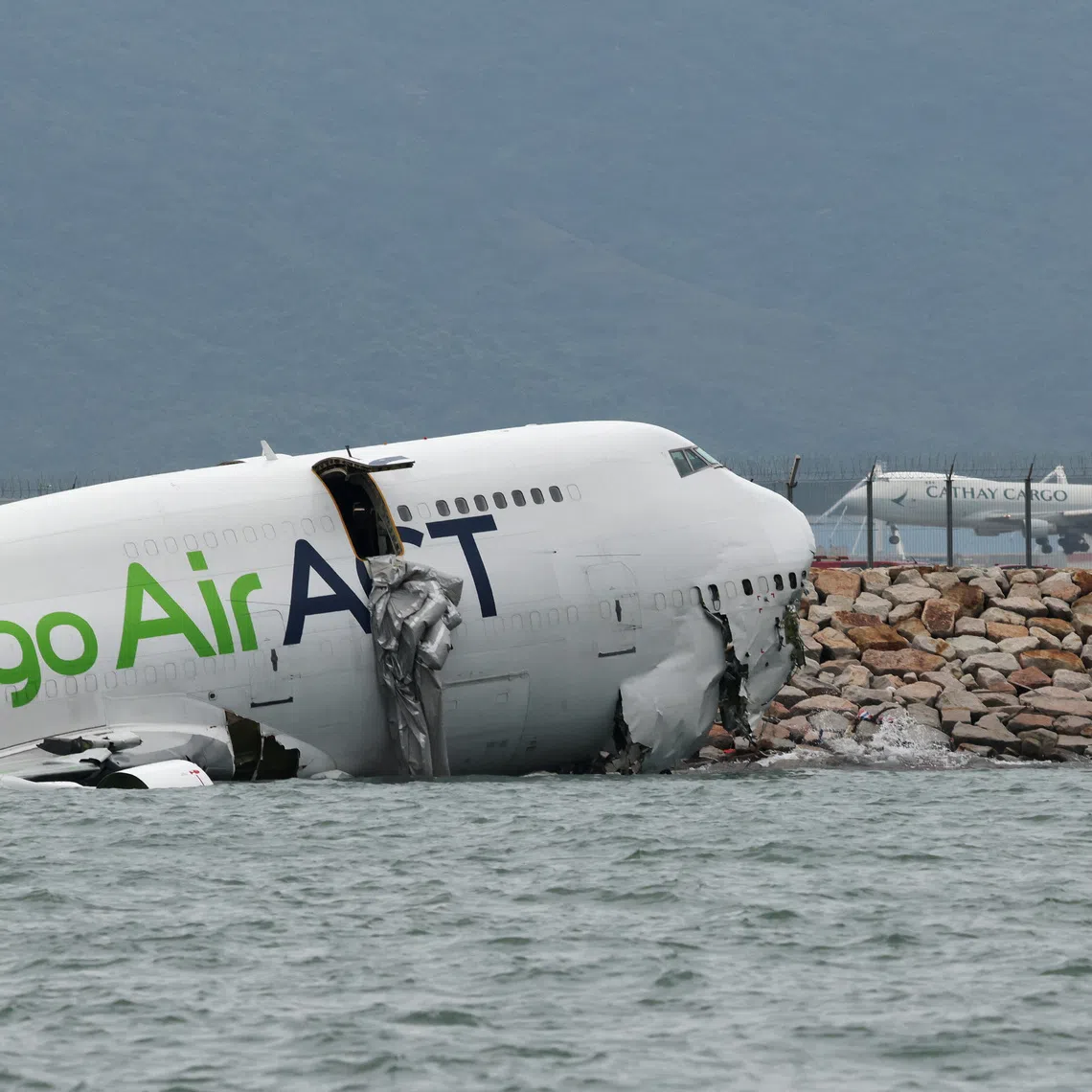 A cargo plane lies partially in the sea after veering off the runway during landing at Hong Kong International Airport in Hong Kong, China, October 20, 2025. REUTERS/Tyrone Siu