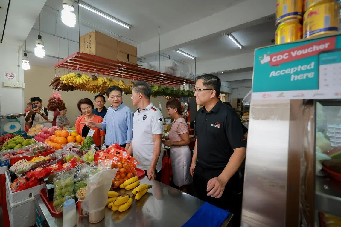 DPM Lawrence Wong (centre, in blue) speaking with a fruit stall owner (in white) with mayors (from left) Low Yen Ling, Desmond Choo, Denise Phua and Alex Yam at the CDC Vouchers Scheme launch on Jan 3.