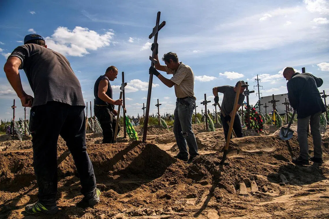 A volunteer placing a cross onto the grave of one of fifteen unidentified people killed by Russian troops in Bucha, Kyiv region, on Sept 2, 2022.