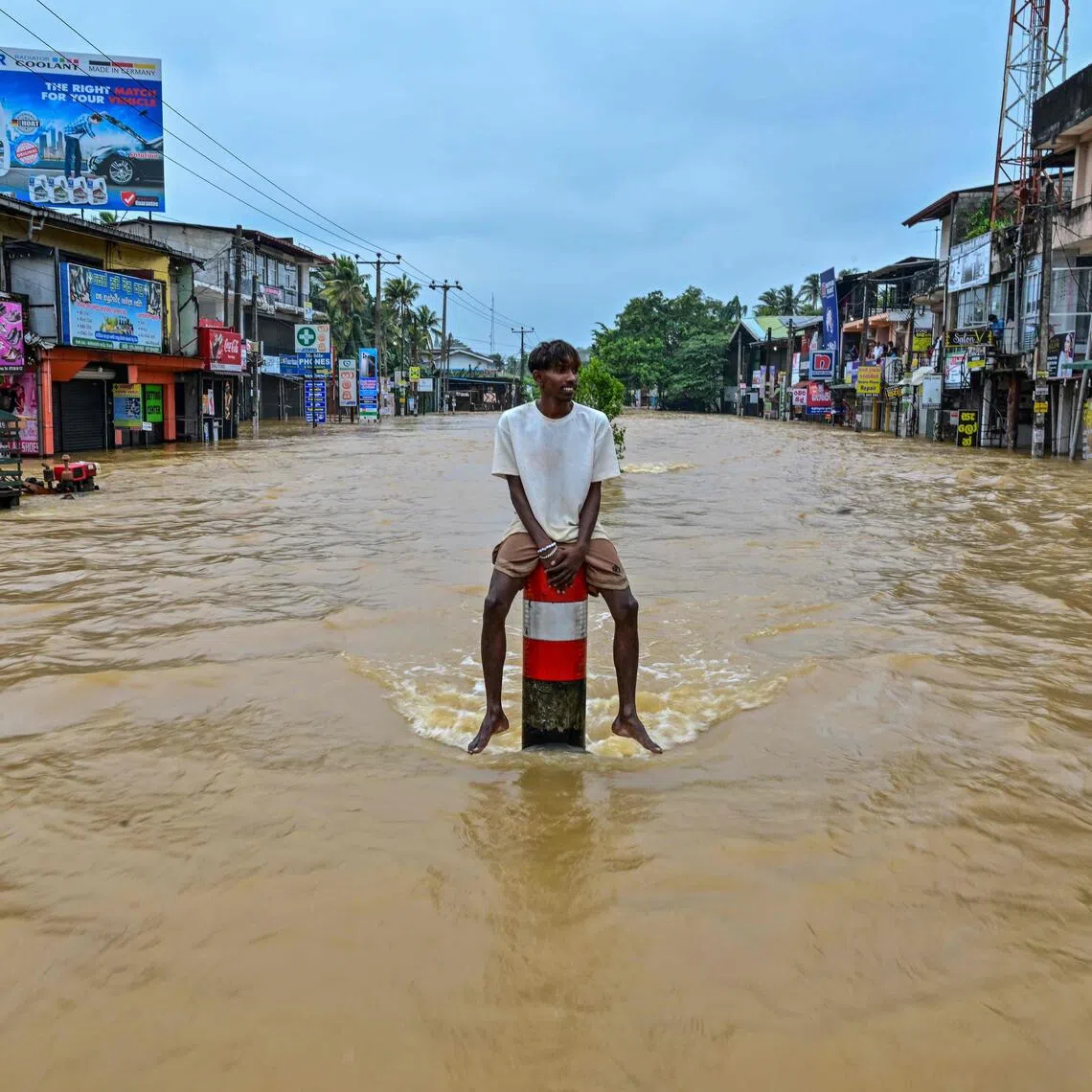 A man sits on a divider in the middle of a flooded road after heavy rainfall in Kaduwela on the outskirts of Colombo on Nov 29, 2025.