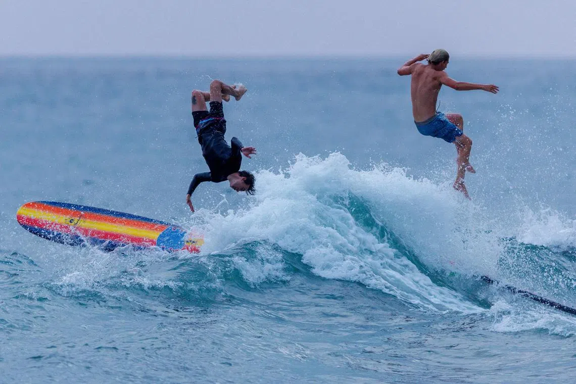 Surfers Sam Paulsen (R) of Encinitas and Sean Bobo of Cardiff flipping off a wave while surfing the high tide backwash along a cliff coastline in Encinitas, California, U.S., August 1, 2023. 