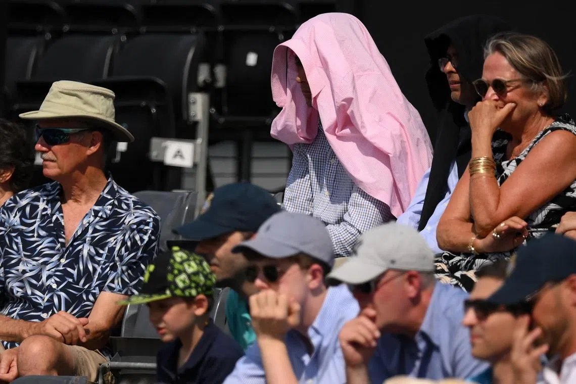 A spectator uses a shirt to cover the head, sheltering from the sun, as they watch Spain's Carlos Alcaraz play against Czech Republic's Jiri Lehecka during the round of 16 men's singles tennis match at the Cinch ATP tennis Championships at Queen's Club in west London on June 22, 2023. (Photo by Daniel LEAL / AFP)