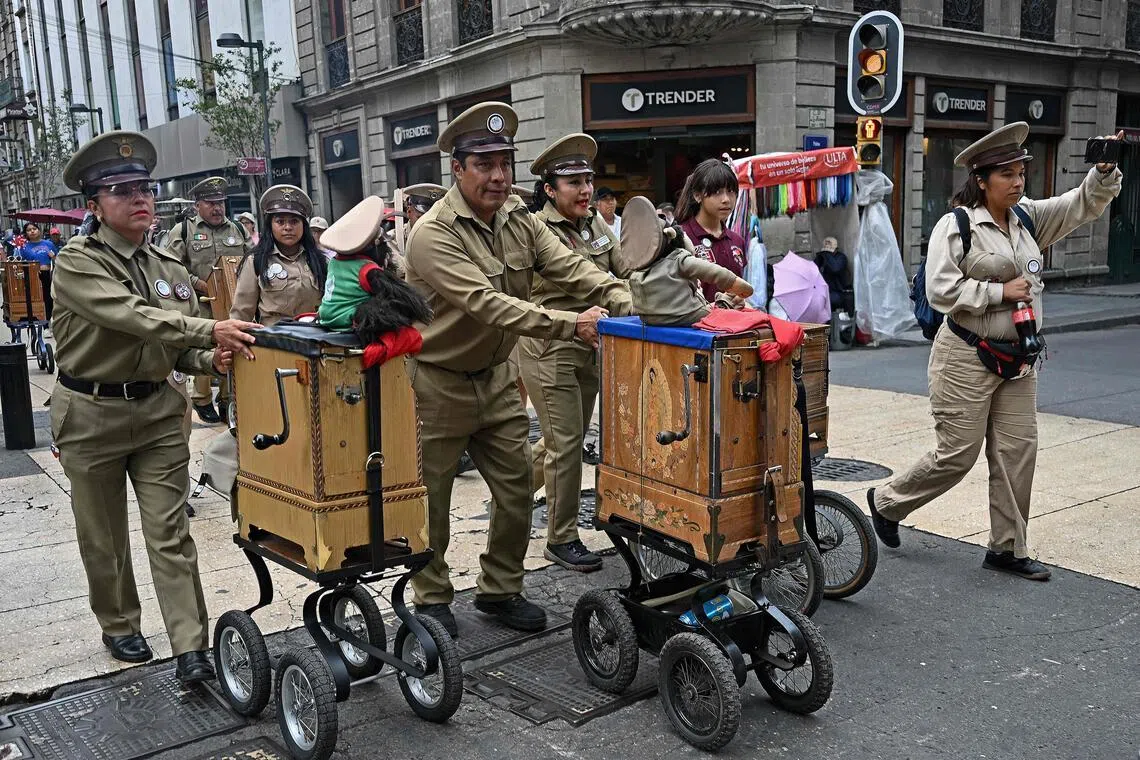 Organ grinders march during an event in Mexico City on May 24, 2026. The traditional instrument, weighing between 24 and 38 kilos, is a wooden box with an internal cylinder, metal pegs which pluck metal teeth to create the music, and a crank that drives it. The instrument has been played by Mexican operators since the late 1800s and is commonly seen in Mexico City’s centre with donations asked by those playing it. (Photo by CARL DE SOUZA / AFP)