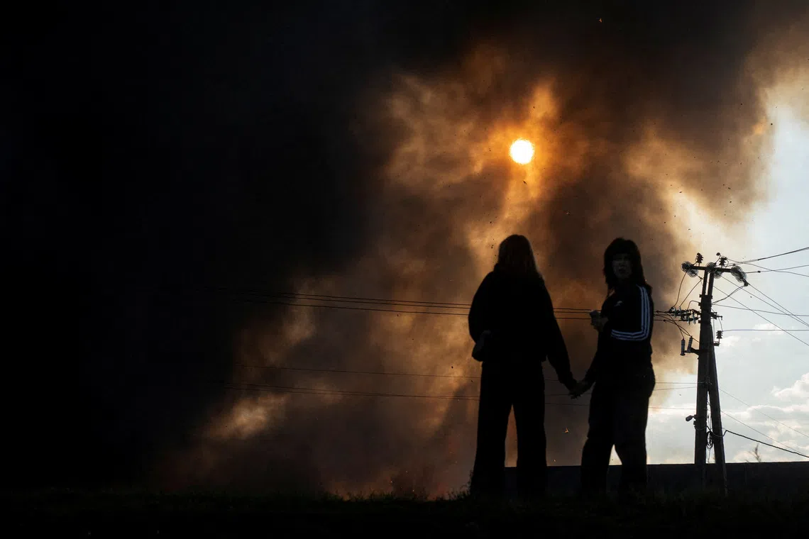 Residents hold hands as smoke rises over a warehouse, which was hit by a Russian drone strike, amid Russia's attack on Ukraine, in Kyiv region, Ukraine, September 20, 2026. REUTERS/Serhii Korovainyi