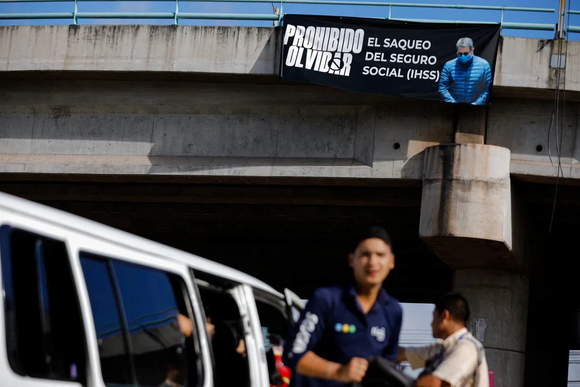 People walk near a banner with a picture of former Honduras' President Juan Orlando Hernandez reading "Never Forget" on Nov 29.