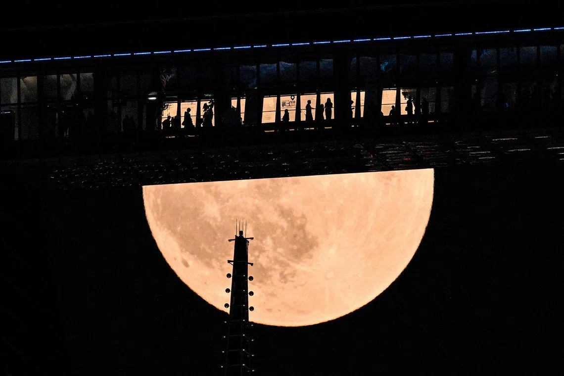 People are seen on a floor of the Shanghai World Financial Centre as a full moon, also known as a blood moon, rises above skyscrapers during a total lunar eclipse in the financial district of Lujiazui in Shanghai on Sept 7, 2025. 