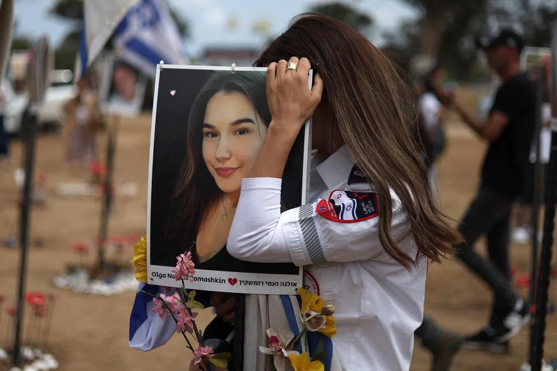A member of an emergency service touching a portrait of a victim, at the memorial site for the victims of the Nova music festival killed in the Oct 7 Hamas attacks, during Israel's Memorial Day, in Re'im, near the border with the Gaza Strip, on May 13, 2024. 