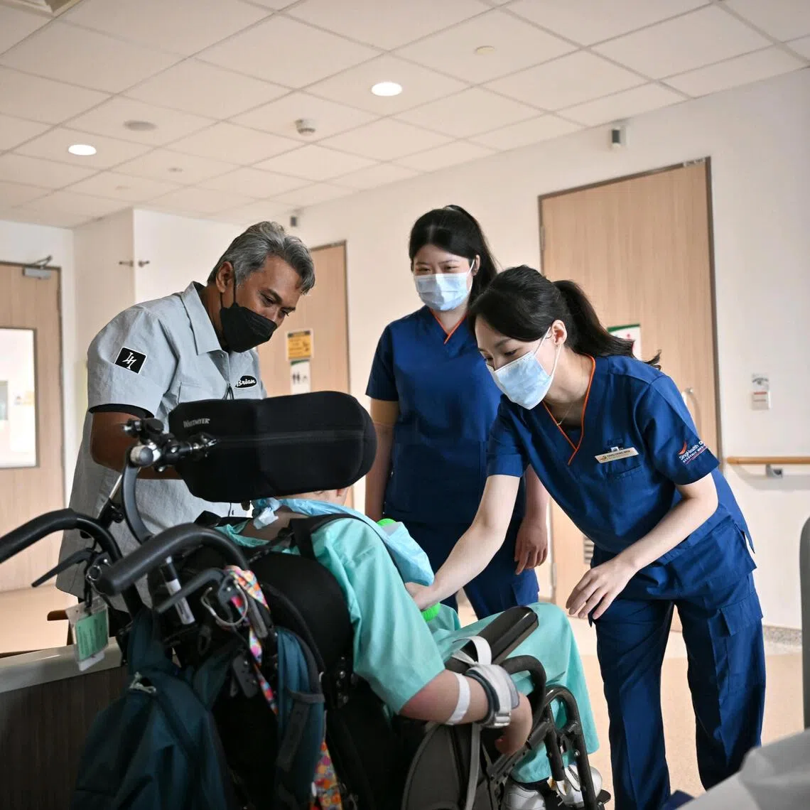 (Left) Mr Mohd Aszrin Ahmad, 51, and his son (seated) Dean Joaquim Mohd Aszrin, 14, with (centre)  physiotherapist Jilene Lau, and occupational therapist Yang Ching Wen, both from Sengkang Community Hospital, at the Paediatric Care ward.