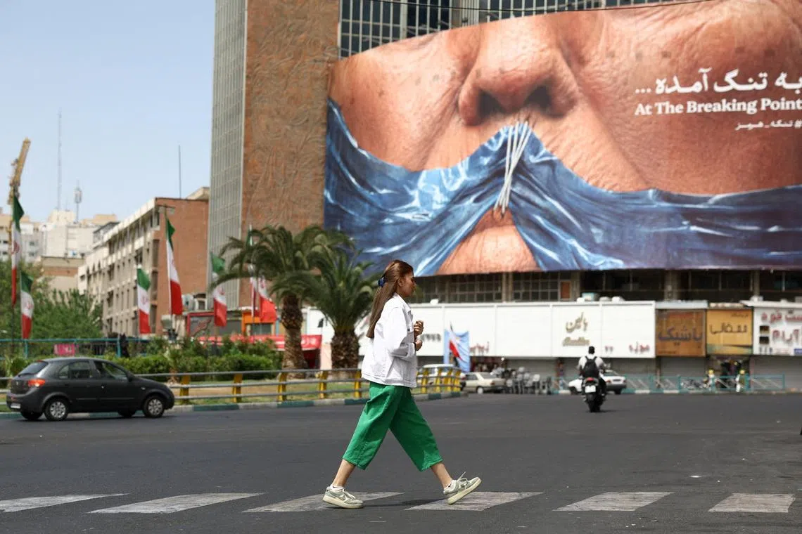 A woman walks past an anti-US billboard depicting US President Donald Trump and the Strait of Hormuz, in Tehran, Iran.