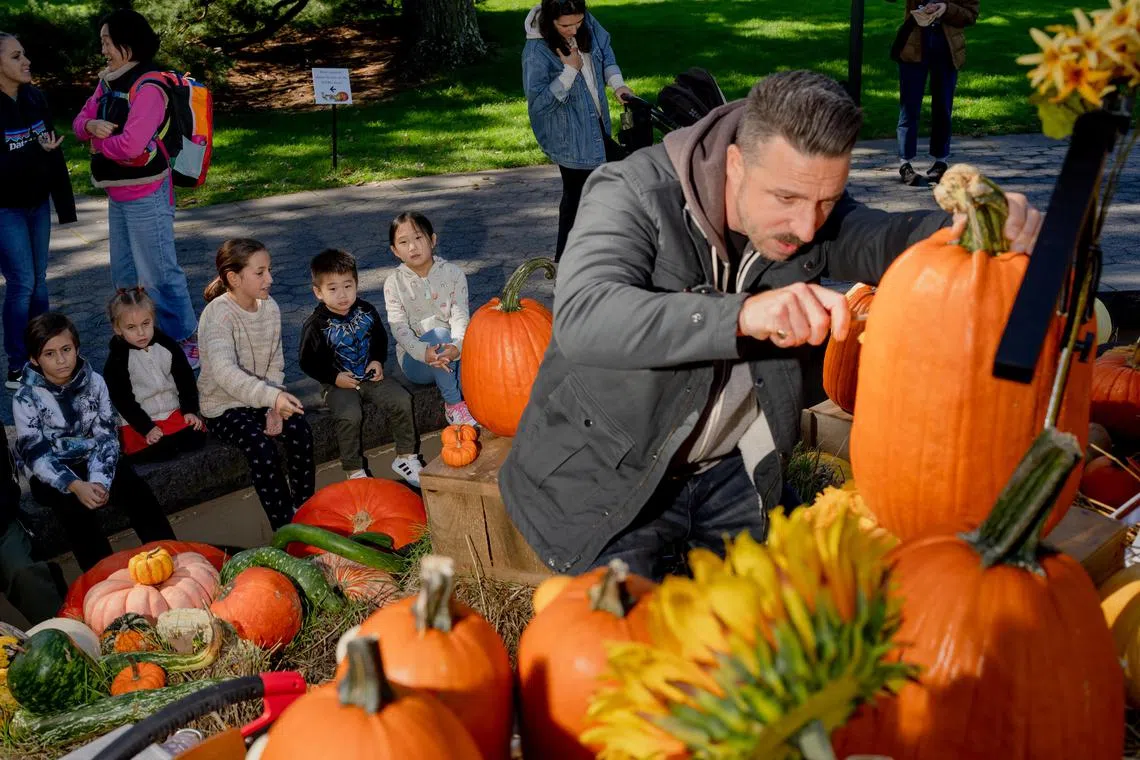 Children watch Adam Bierton carve a pumpkin at the New York Botanical Garden, where he has been doing weekend demonstrations since 2018, in New York, Oct. 9, 2023. Bierton is allergic to pumpkins, but that does not stop him from carving dozens each fall, the most of intricate of which can cost $5,000. (Amir Hamja/ The New York Times)
