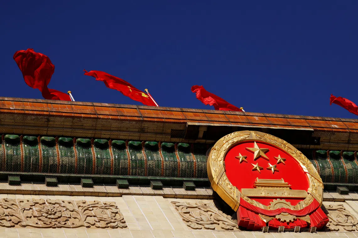A Chinese flag flutters above the national emblem on the Great Hall of the People before the opening session of the National People's Congress (NPC) in Beijing, China March 5, 2022. REUTERS/Carlos Garcia Rawlins