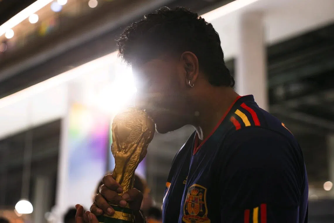 A Spanish fan posing for a photo with a replica of the World Cup trophy after the full-time whistle during the live screening of the FIFA World Cup 2026 final between Argentina and Spain at Our Tampines Hub in the early hours of July 20, 2026. Spain won the game 1-0. ST PHOTO: BRIAN TEO
