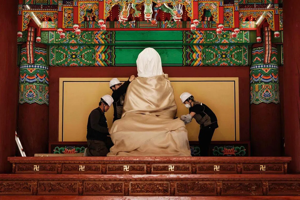 TOPSHOT - Members of the Gyeongbuk Seobu Cultural Heritage Care Center wrap a Buddha statue with cotton cloth and a fire-retardant blanket after evacuating all other items the night before, during preparations for the possibility of a wildfire advancing towards Gounsa Temple in Uiseong on March 25, 2025. Deadly wildfires in South Korea worsened overnight, officials said on March 25, as dry, windy weather hampers efforts to contain one of the country's worst-ever fire outbreaks. (Photo by YASUYOSHI CHIBA / AFP)