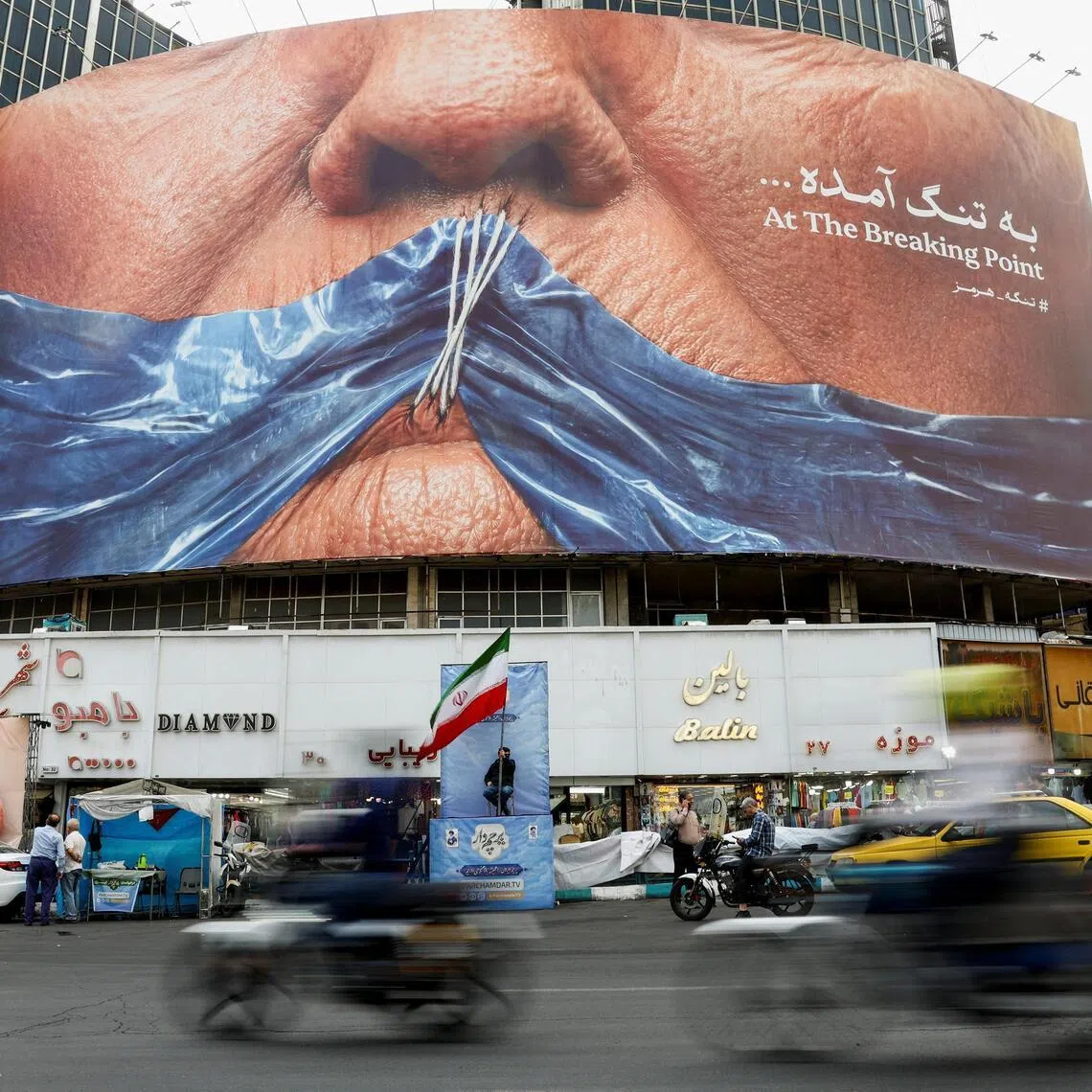 People drive past a billboard depicting US President Donald Trump and the Strait of Hormuz, in Tehran, Iran.