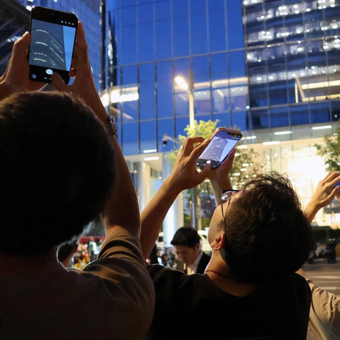 People point their mobile phones at CITIC Tower, also known as China Zun, where damage is visible on a high floor of the exterior in Beijing.
