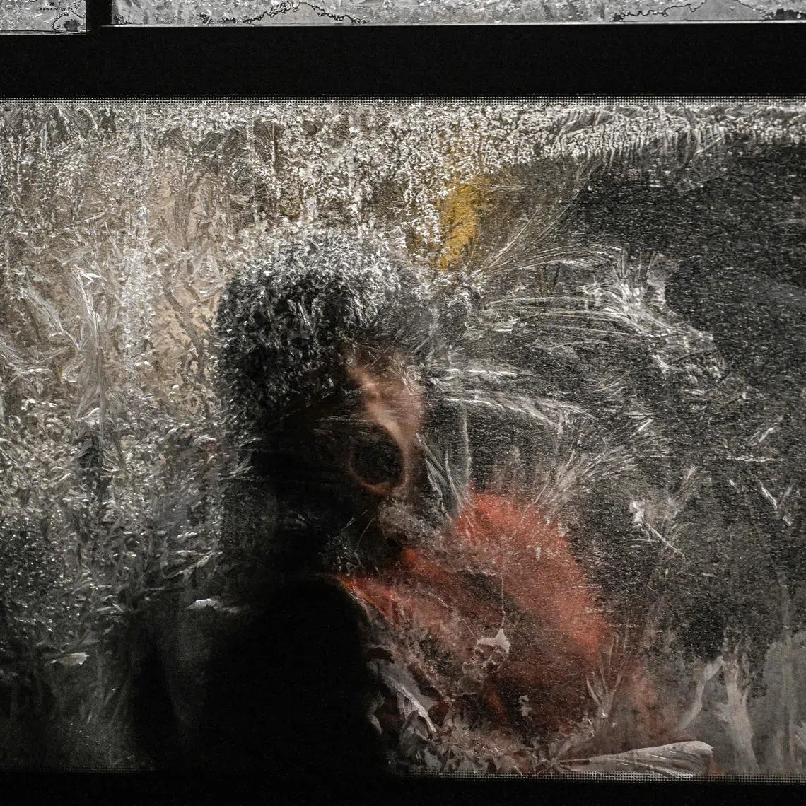 A boy trying to remove frost from a frozen window, as he rides a bus during a winter evening in Kyiv, on Jan 15, 2026, amid the Russian invasion of Ukraine.