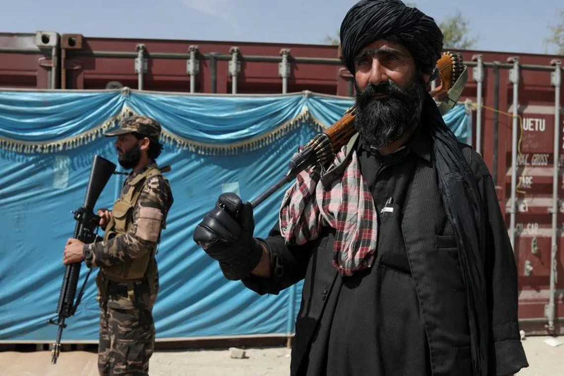 FILE PHOTO: Taliban fighters stand guard while people wait to receive sacks of rice, as part of humanitarian aid sent by China, at a distribution centre in Kabul, Afghanistan, April 7, 2022. REUTERS/Ali Khara/File Photo