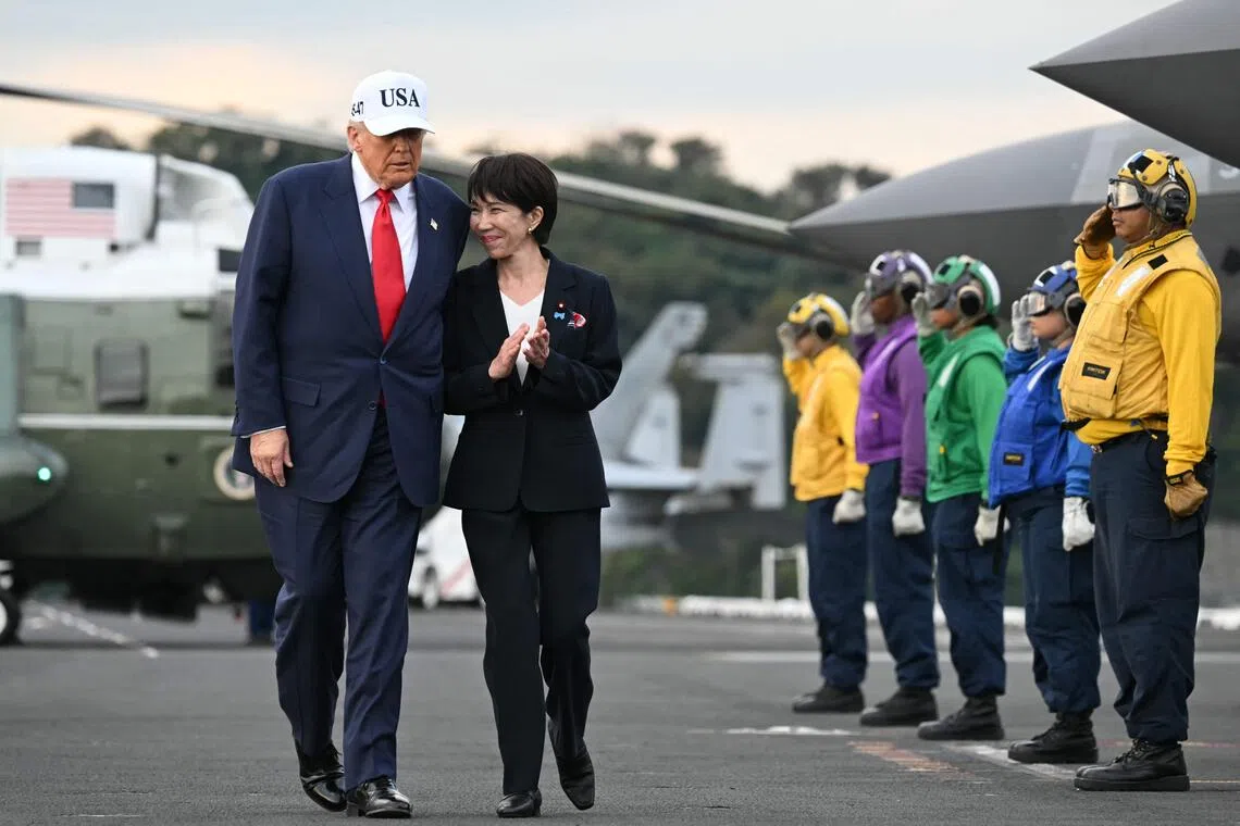 US President Donald Trump (L) and Japan's Prime Minister Sanae Takaichi (2nd L) walk past rainbow sideboys in salute on board the USS George Washington aircraft carrier at the US naval base in Yokosuka, Japan, on October 28.
