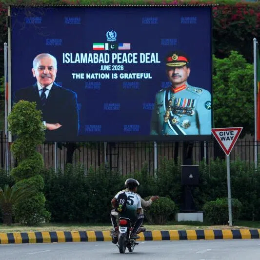 Men riding a motorcycle past a roadside billboard displaying portraits of Pakistan's Chief of Army Staff Field Marshal Asim Munir and Prime Minister Shehbaz Sharif, following a deal between the US and Iran, in Islamabad, on June 16.