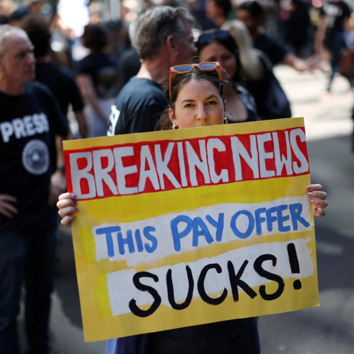 A woman holds a placard as ABC staff and journalists strike outside the national broadcaster's headquarters in Sydney, Australia, March 25, 2026. REUTERS/Hollie Adams
