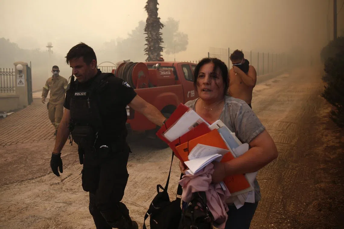 A policeman evacuating a local resident due to a fire that broke out in eastern Attica, Greece, on June 19, 2024. 
