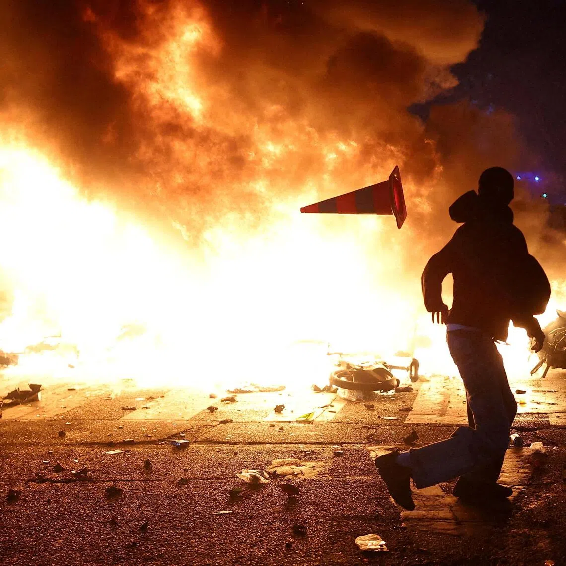 A man throws a plastic traffic cone through a burning barricade amid clashes during demonstrations against the cost of living and rising fuel prices in Paris on Oct 17.