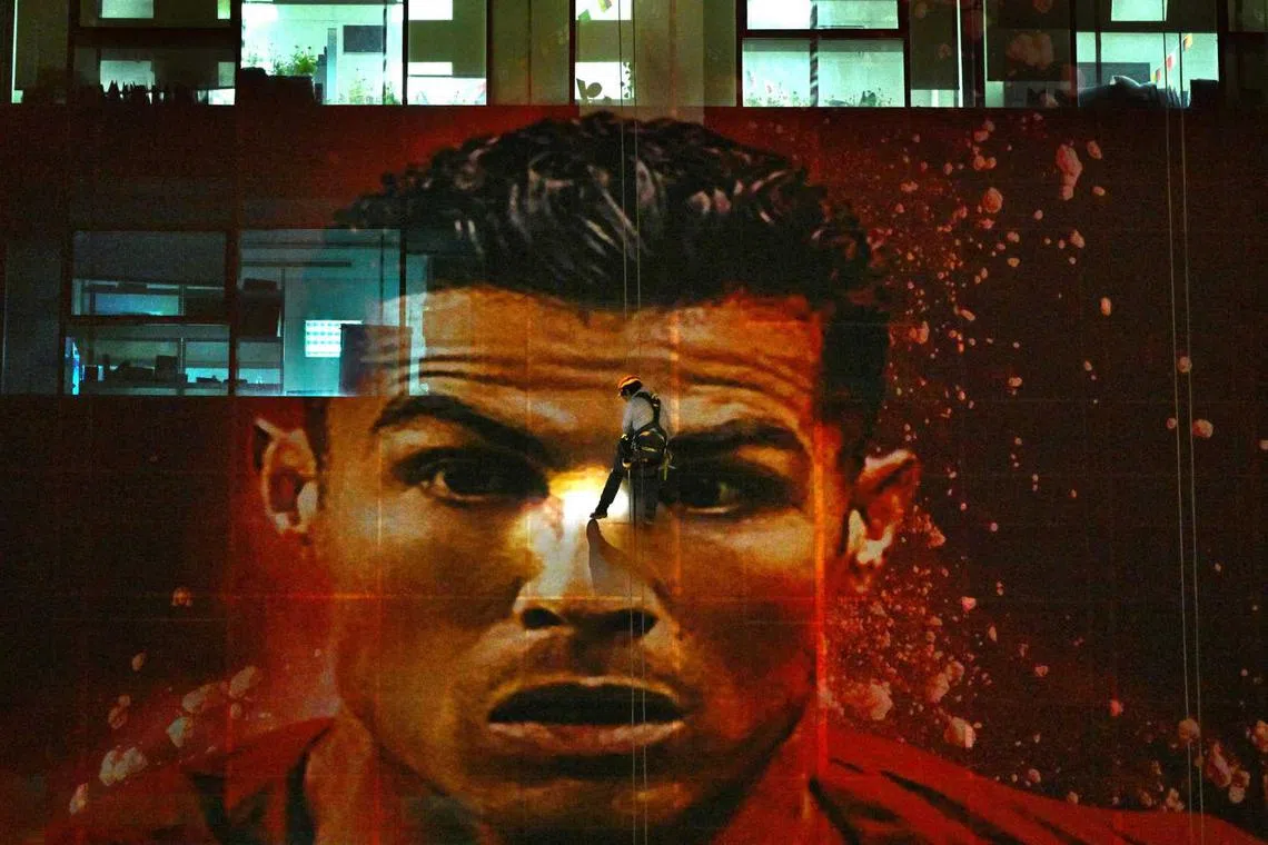 A worker installs a large picture of Portugal's forward Cristiano Ronaldo on a building in Doha on Nov 20, 2022, during the opening day of the Qatar 2022 World Cup football tournament. 