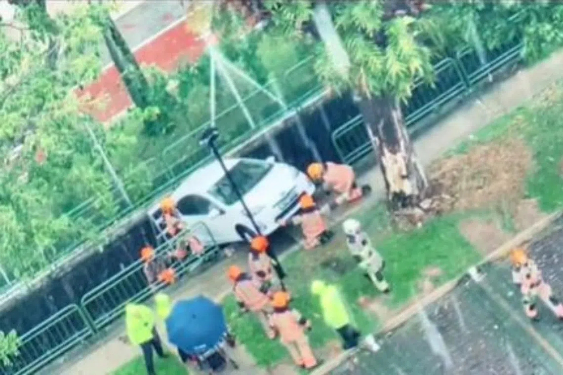SCDF officers are seen near a car that appears to be perched on the edge of a pavement at Lorong 8 Toa Payoh.