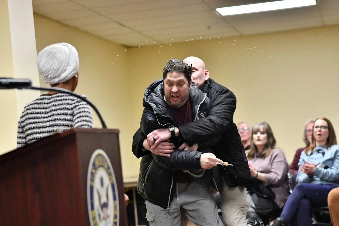 A man is tackled after spraying an unknown substance at US Representative Ilhan Omar (left) during a town hall in Minneapolis on Jan 27.