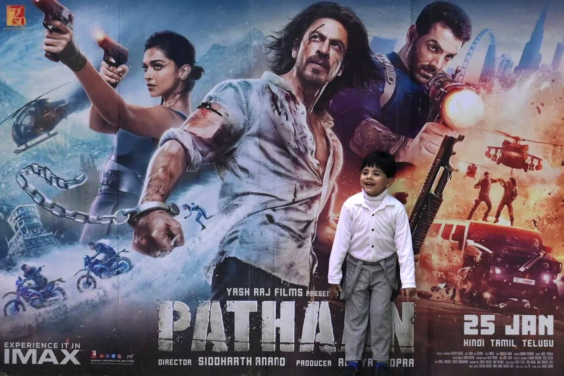A boy plays in front of a poster of the Bollywood movie 'Pathaan' outside a cinema hall in Prayagraj on January 25, 2023. - Bollywood megastar Shah Rukh Khan returned to the silver screen on January 25 for the first time in four years with an action-packed rollercoaster film that has sparked ire from Hindu right-wingers. (Photo by SANJAY KANOJIA / AFP)