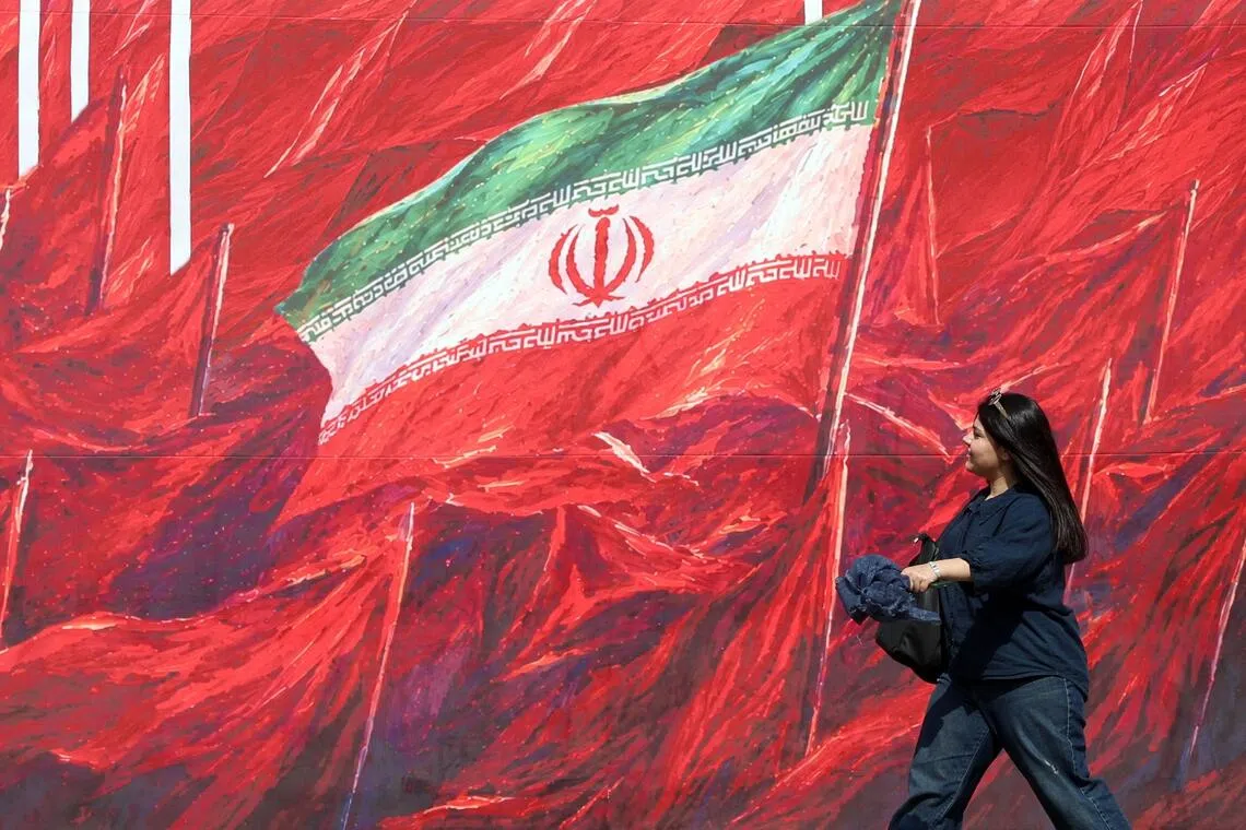 An Iranian woman walking past a banner in Tehran on Oct 14 featuring Iran’s national flag.