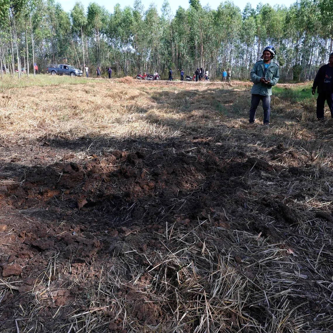 People examine an impact crater in a field following clashes along the Thailand-Cambodia border in Thailand's Sisaket province on Dec 9, 2025.  